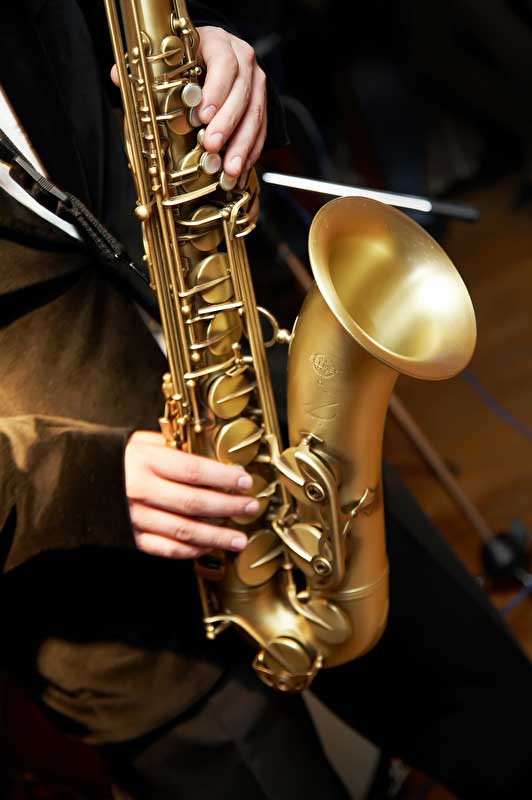 Das Bild zeigt ein Saxofon und zwei Hände welche es gerade spielen.
