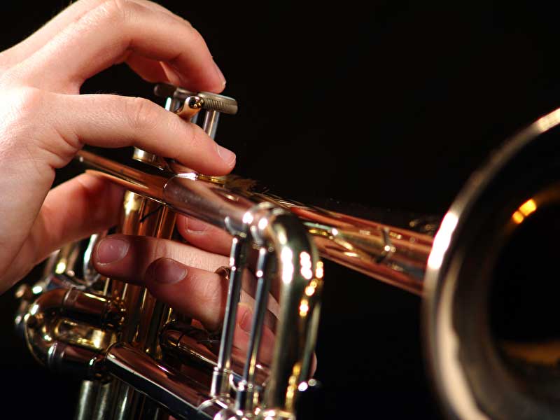 Das Bild zeigt eine Trompete in Nahaufnahme und Finger welche diese spielen.
