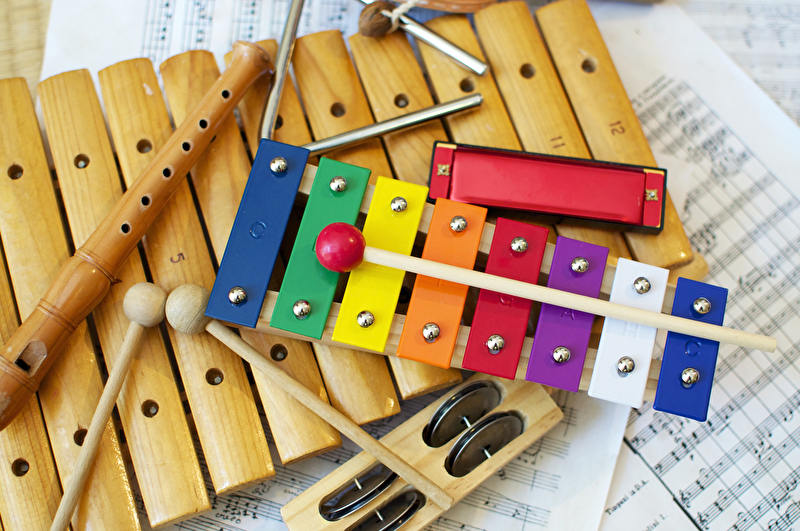 Dieses Bild zeigt einige typische bunte Musikinstrumente wie sie vor allem von Kindern verwendet werden. Die Instrumente stehen auf einer Partitur.